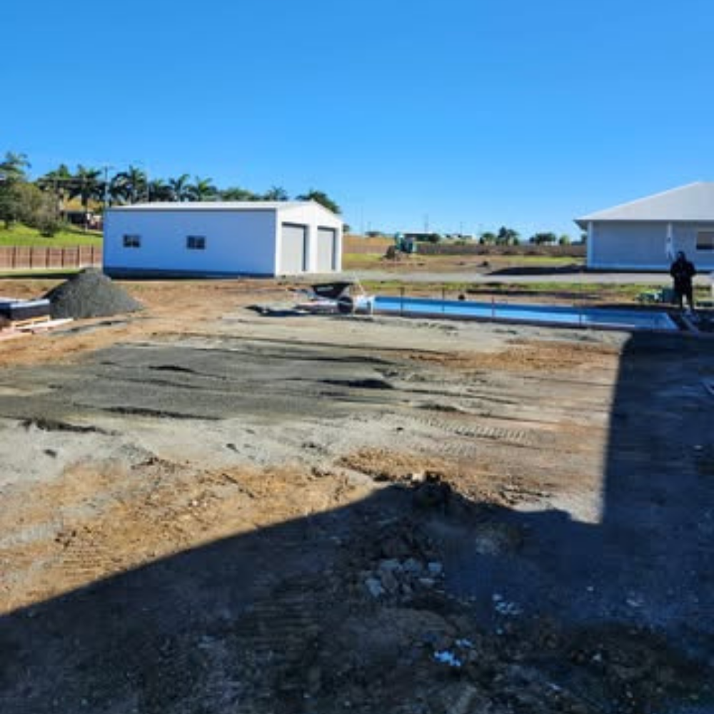 Construction site with a partially built pool and surrounding area under a clear blue sky.