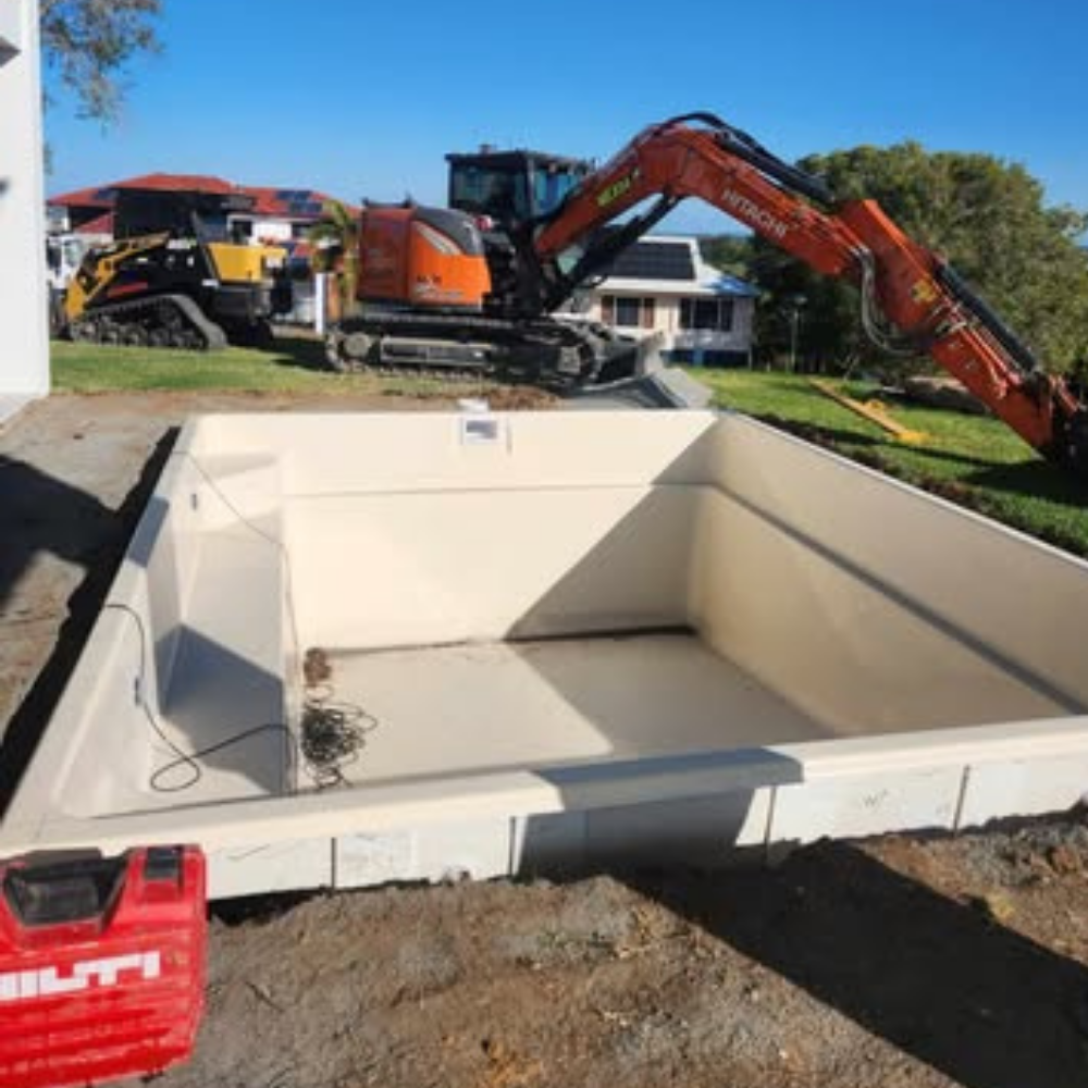 Pool recently installed in the ground with an excavator in the background