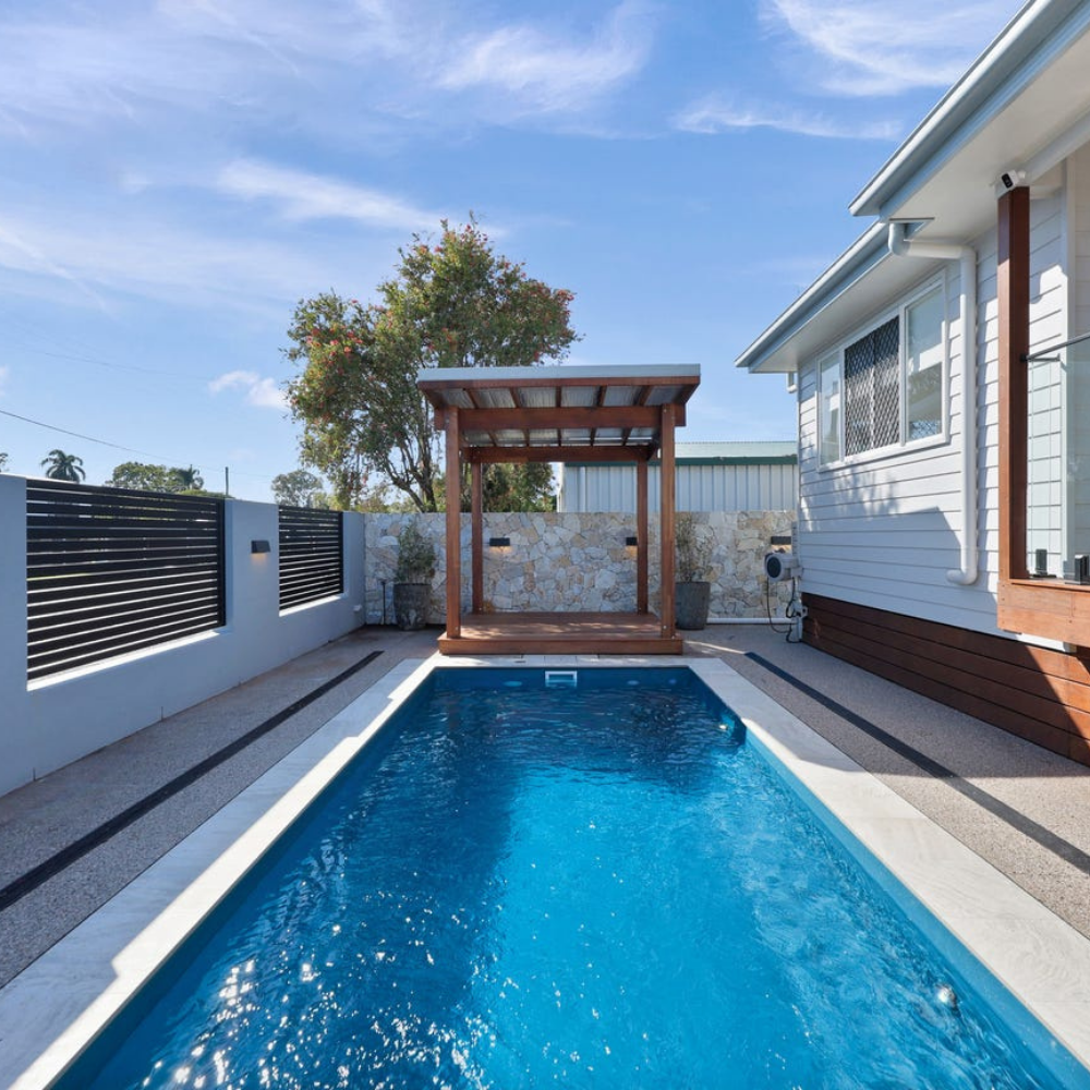 Swimming pool with a wooden pergola and house in the background