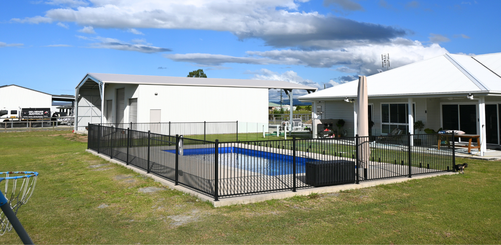 Swimming pool with a fence in a residential area under a blue sky.