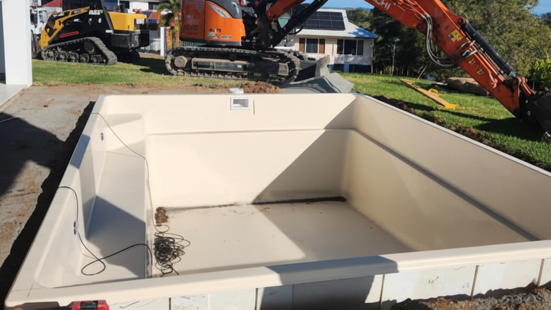 Pool recently installed in the ground with an excavator in the background 